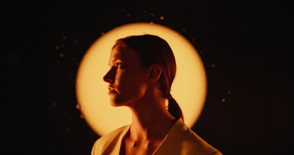 Expressive Portrait of Young Woman Wearing White Clothes Posing for Camera, Performing as a Fashion Model in a Dark Space with Rain and Warm Light