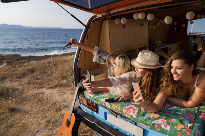 Relaxed girl friends taking selfie comfortable placing on trunk of blue car