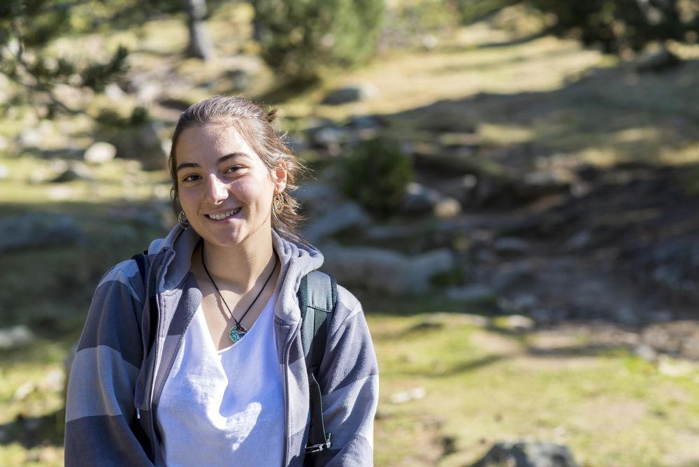 Happy young woman standing in green woods with boulders on ground