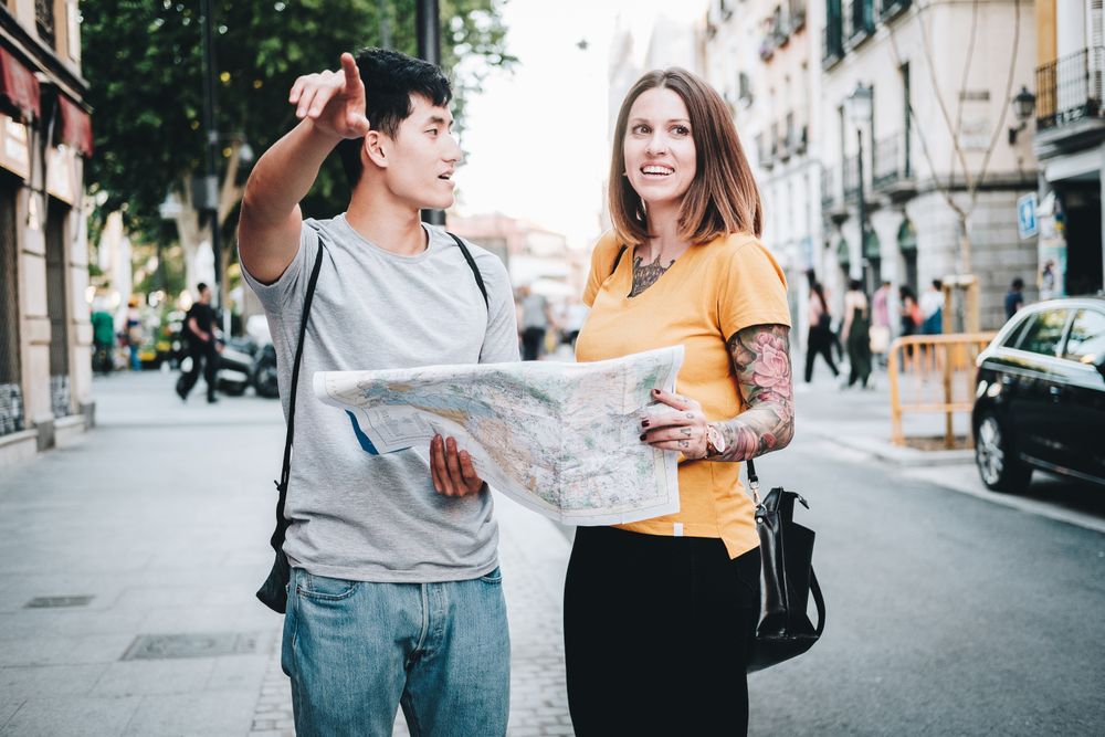 Joyful multiracial tourists checking map and standing on urban street