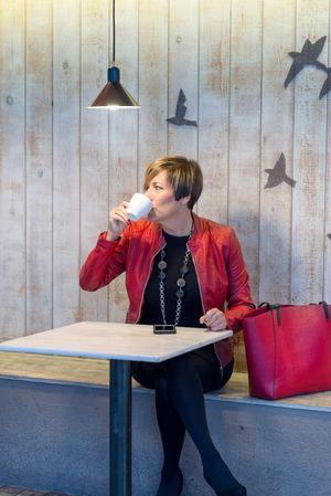 Woman in red coat sitting in cafe sipping coffee