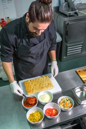 Professional male chef preparing pizza with fresh ingredients in commercial kitchen