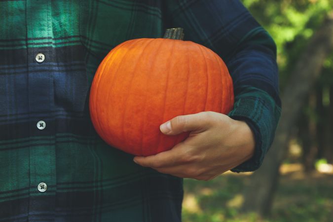 Woman in checkered shirt hold pumpkin outdoor