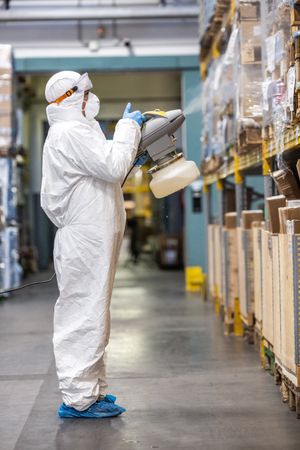 Man in PPE sanitizing shelves in warehouse during lockdown