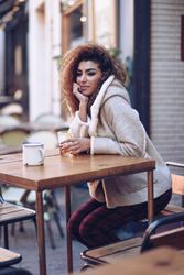 Contemplative woman sitting at wooden table of outdoor bar with drink
