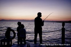 Silhouette of man holding fishing rod and two boys standing by seashore during sunset bYrYN0