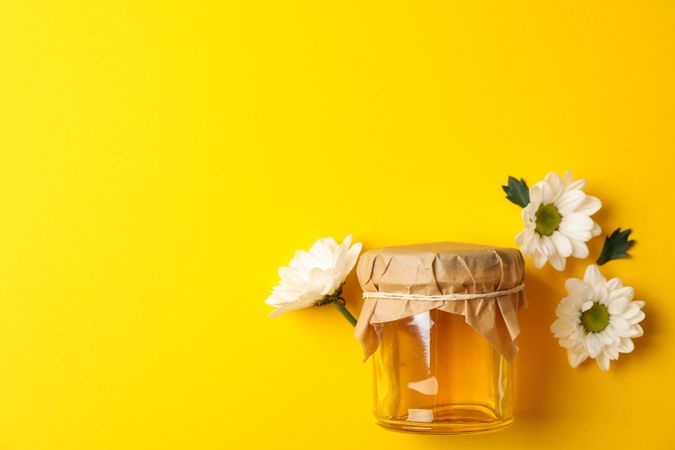 Glass jar with honey and chamomile on yellow background, space for text