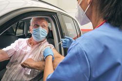 Crop doctor vaccinating mature man in car with syringe