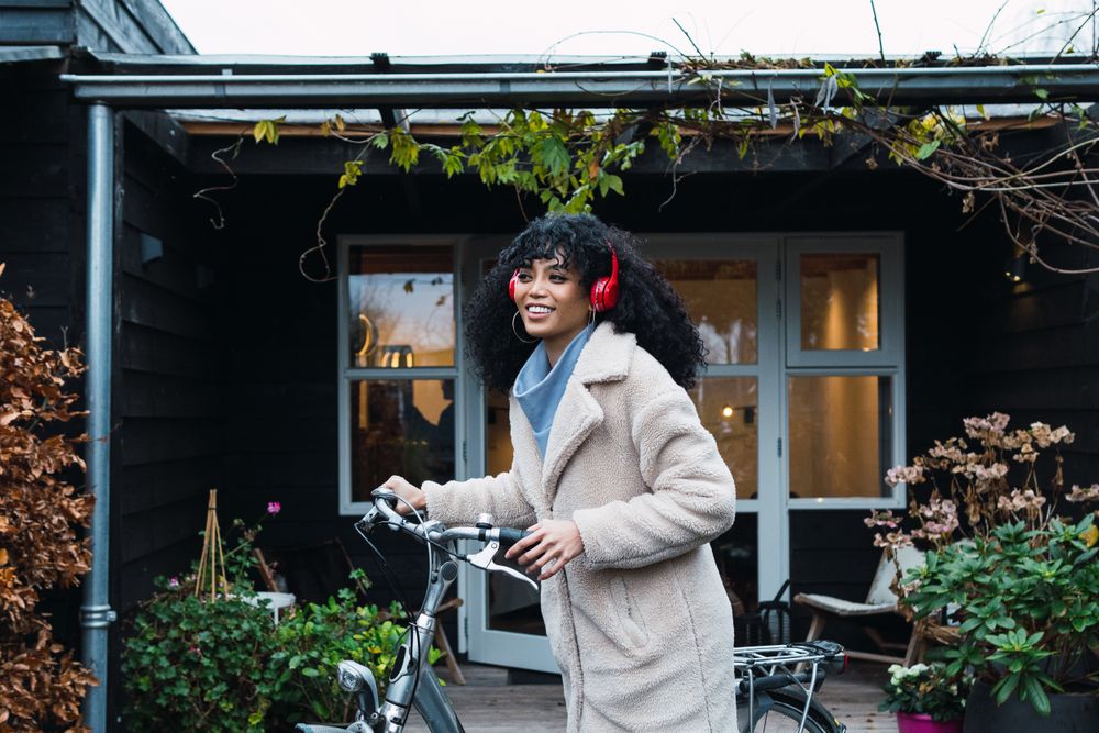 Cheerful Black woman in headphones with bicycle
