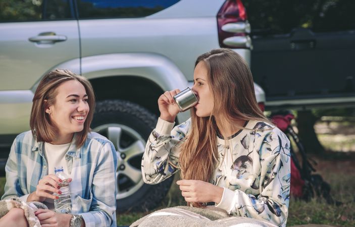 Woman drinking cup of coffee with friend in campsite
