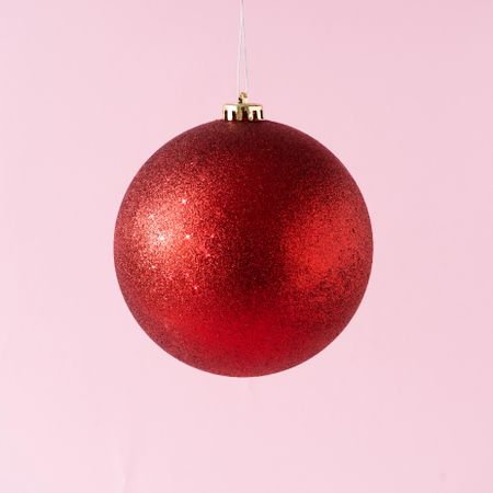 Red glitter Christmas bauble on pastel pinks background