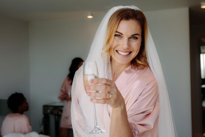 Happy young woman drinking champagne at bachelorette party in bedroom