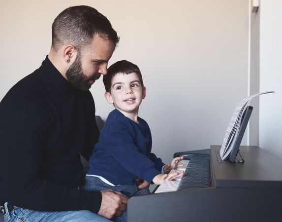 Father teaching son to play piano
