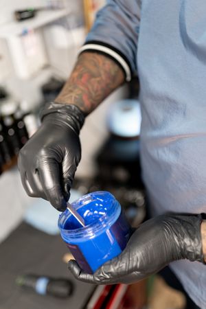 A tattoo artist is picking up some blue skin vaseline before work