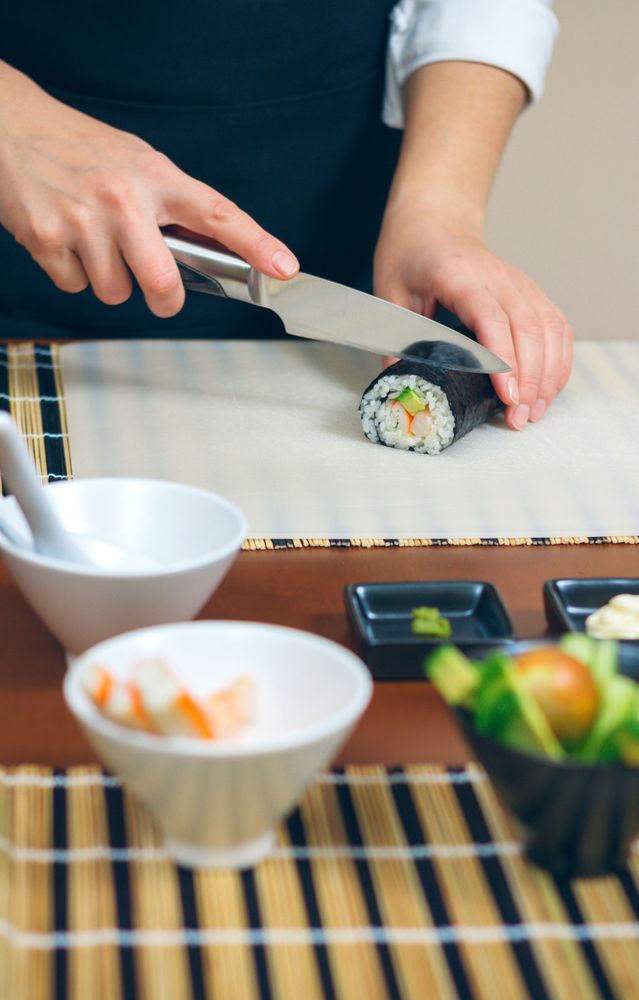 Female chef cutting Japanese sushi rolls with rice, avocado and shrimps in nori seaweed sheet