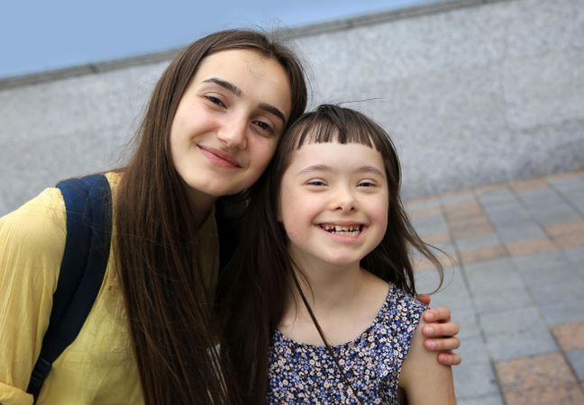 Two sisters smiling and hugging together outdoors