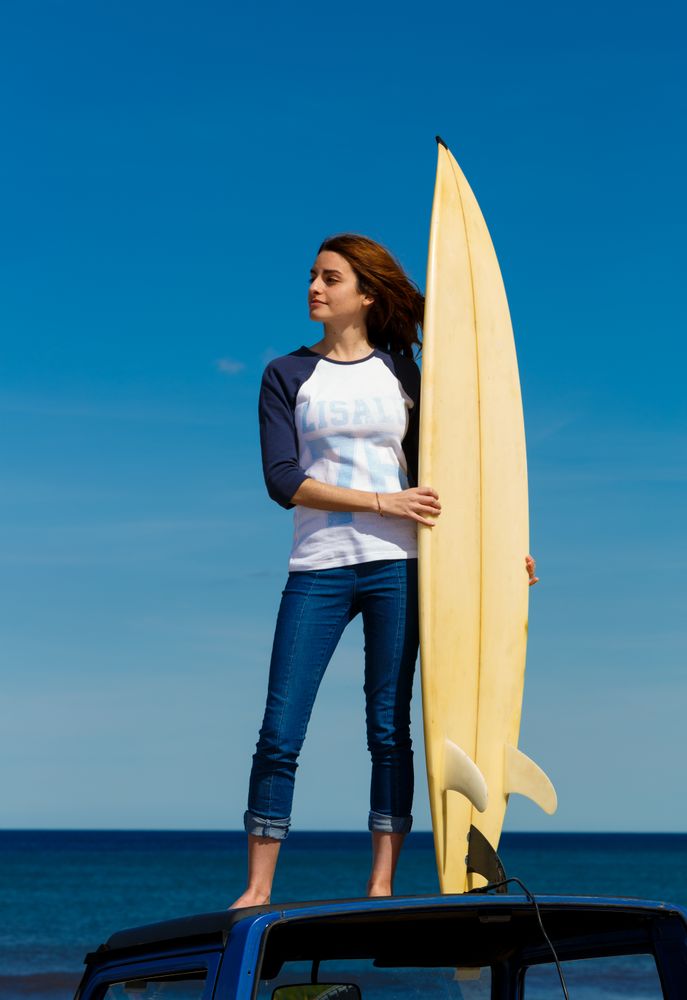 Woman with surfboard standing on roof of car