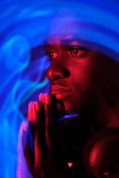 Pensive Black man in headphones on neck in neon illumination
