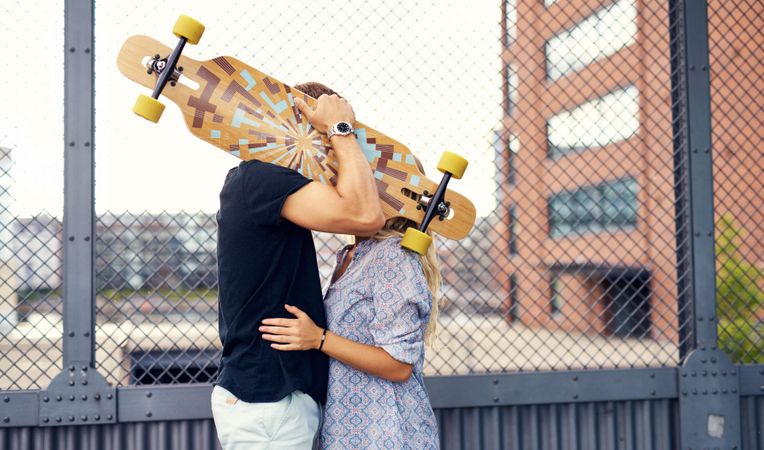 Man and woman kissing behind a skateboard
