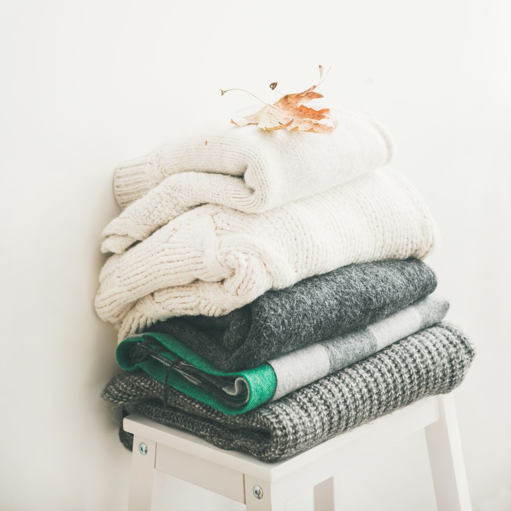 Pile of clean, folded sweaters on light background, square crop