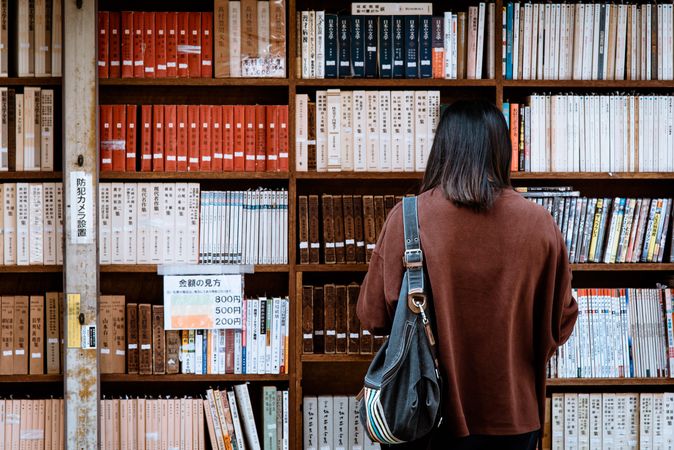 Back view of woman in brown jacket standing beside book selves in the library
