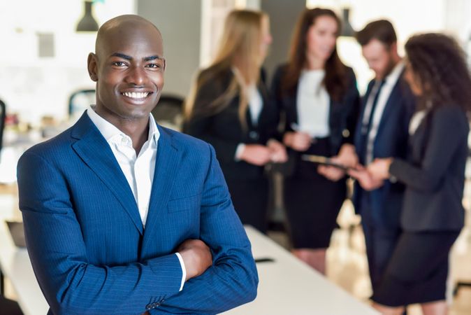 Black male business leader standing in foreground of busy office