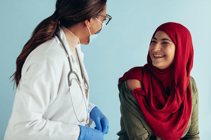 Smiling woman in hijab talking with female doctor in face mask