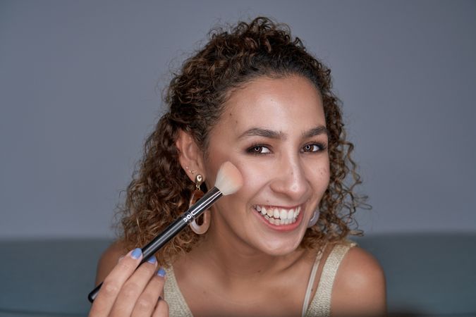 Cheerful woman shading glowing highlighter powder with brush on