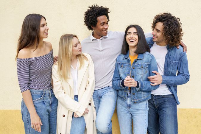 Happy friends posing for portrait leaning against a yellow wall