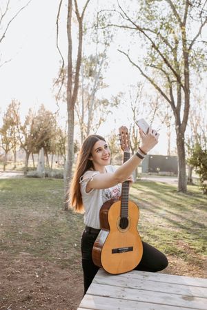 Smiling female guitarist taking selfie in park