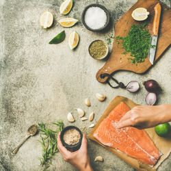Salted salmon fillet with fresh herbs, limes, onions, bread board, hand with salt, copy space