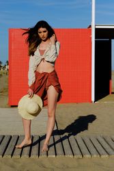 A long hair fashion model with a hat at the beach in front of a red wall