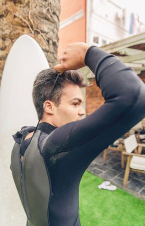 Young male surfer with board closing wetsuit