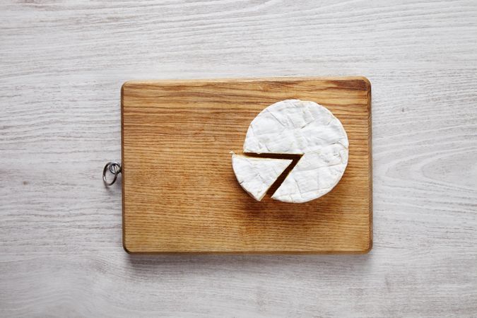 Whole wheel of brie cheese with chunk cut out on wooden board