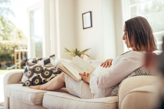 Pregnant woman relaxing on sofa reading  book