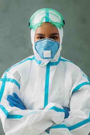 Black female medical professional in hazmat suit with her arms crossed, vertical