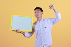Portrait of a young man in yellow backdrop holding a blank note board