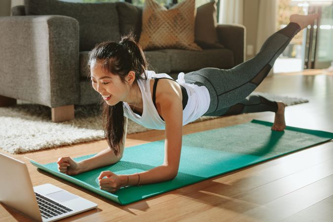 Smiling woman exercising at home and watching training videos on laptop