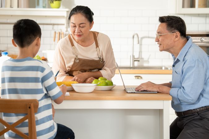 Asian grandmother watching and talking with grandson while doing homework