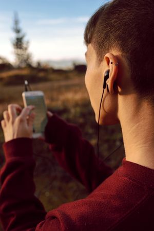 Young woman with piercing listening music on smartphone on hill