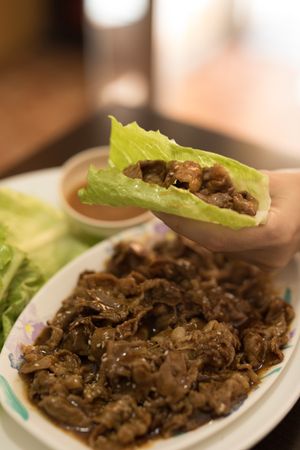 Hand holding meat wrapped in lettuce in restaurant