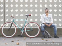 Exasperated male sitting with bike parked in front of patterned cement wall 4NGDDb