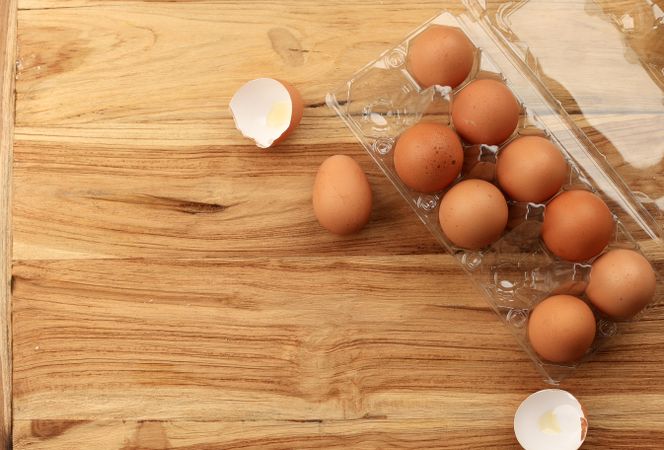 A dozen eggs with a few cracked on wooden table