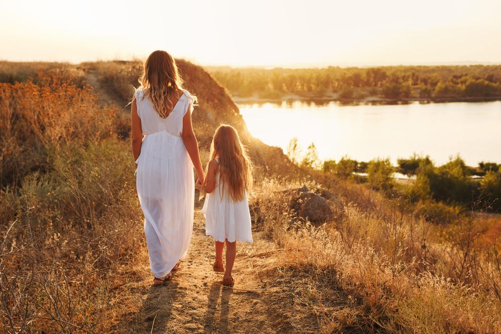 Back of woman and female child in summer walking by the river at dusk