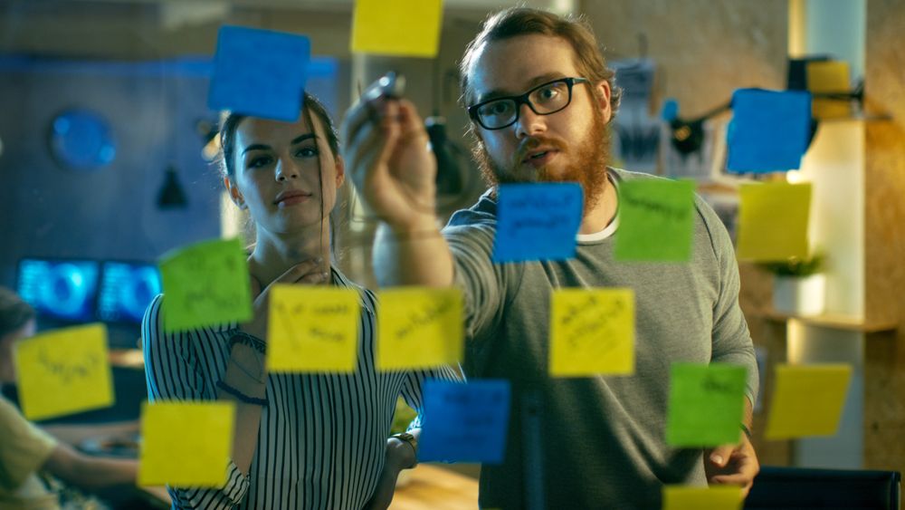 Male and Female Designers Discuss and Outline They're Project with Sticky Notes on a Glass Wall.