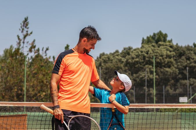 Father and son playing tennis together on a dirt court