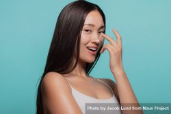 Woman applying moisturizer cream on her face against blue background 0KEwV4