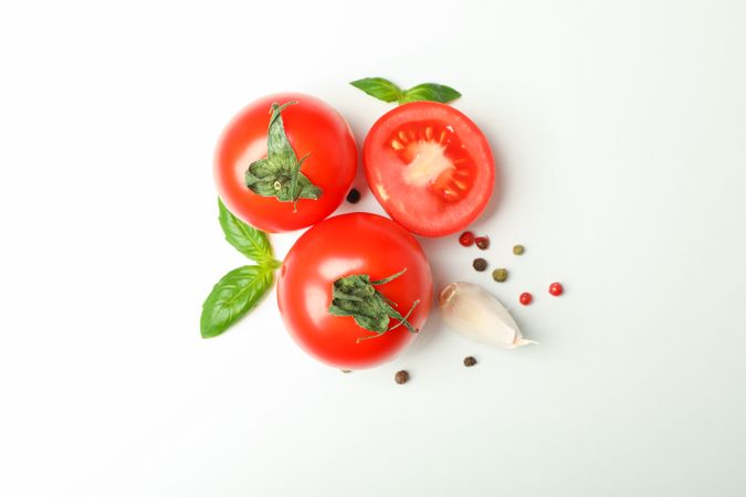 Fresh cherry tomatoes with basil, pepper and garlic on plain background, space for text and top view. Ripe vegetables