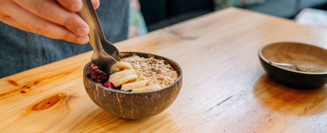 Banner of chef preparing vegetarian breakfast putting banana slices on bowl using metal tongs.