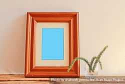 Rectangular wooden picture frame on wooden desk with branch in glass mockup 5adNW0